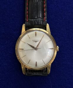 RELOJ LONGINES DE CUERDA. CON PULSERA DE CUERO NEGRO Y DETALLES EN ROJO. EN ORO 18KTS.