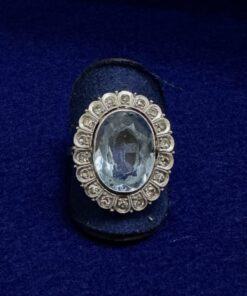 Sortija con topacio azul central y orla de brillantes, montada en oro blanco de ley 18kts.