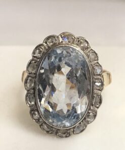 Sortija con piedra azul y orla de diamantes con vistas en plateado en oro de ley 18 kts, presenta calado con motivos de corazón en la parte trasera