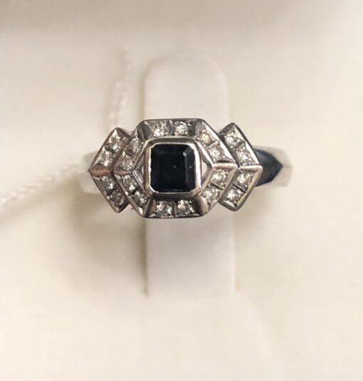 Sortija moderna de estilo Art Decó con 0'40 cts de brillantes y un zafiro central en talla carré de 0'30 cts en oro blanco de ley 18 kts.