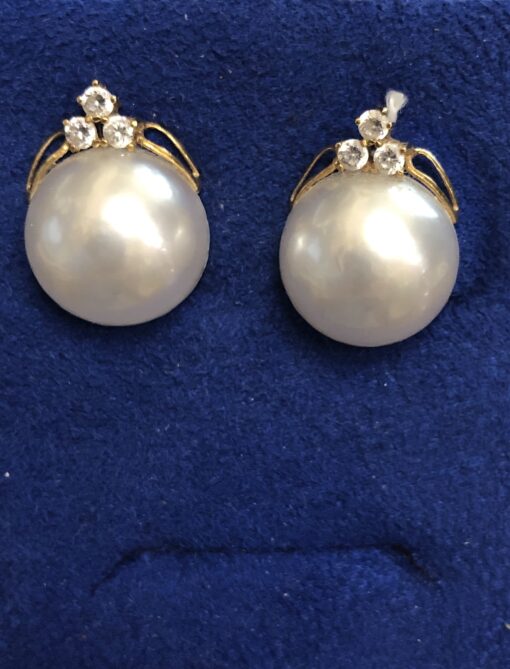 Pendientes con medias perlas coronadas con 3 circonitas y cierre omega, en oro amarillo de ley 18 kts.