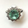 Sortija en forma de rosetón con esmeralda central de 2'10 cts y orla de brillantes de 0'60 cts en total, realizada en oro blanco de ley 18 kts