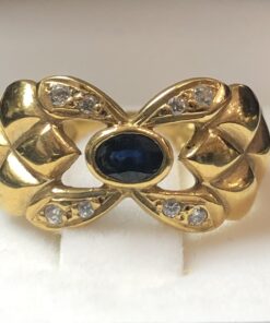 Sortija ancha con motivos calados y zafiro central, aderezada con circonitas, realizada en oro amarillo de ley 18 kts.