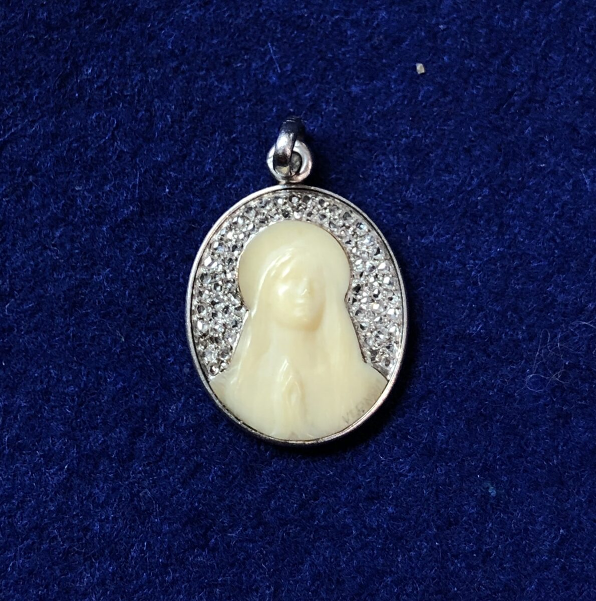 Medalla modernista de ppos. del siglo XX, realizada con retrato de la Virgen tallado en hueso y cuajada con 0'40 cts de brillantes en oro blanco de ley 18 kts. Firmada por el escultor francés F. Vernon