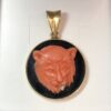 Colgante con cabeza de león tallada en coral sobre placa de ónix en oro de ley 18 kts.