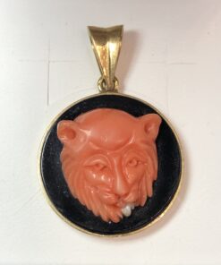 Colgante con cabeza de león tallada en coral sobre placa de ónix en oro de ley 18 kts.