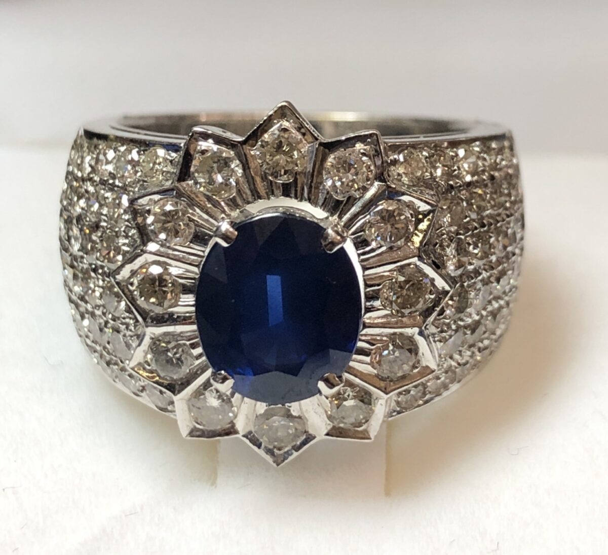 Sortija ancha con zafiro central de 2 cts en rosetón, enriquecida con 1'76 cts de brillantes, realizada en oro blanco de ley 18 kts.