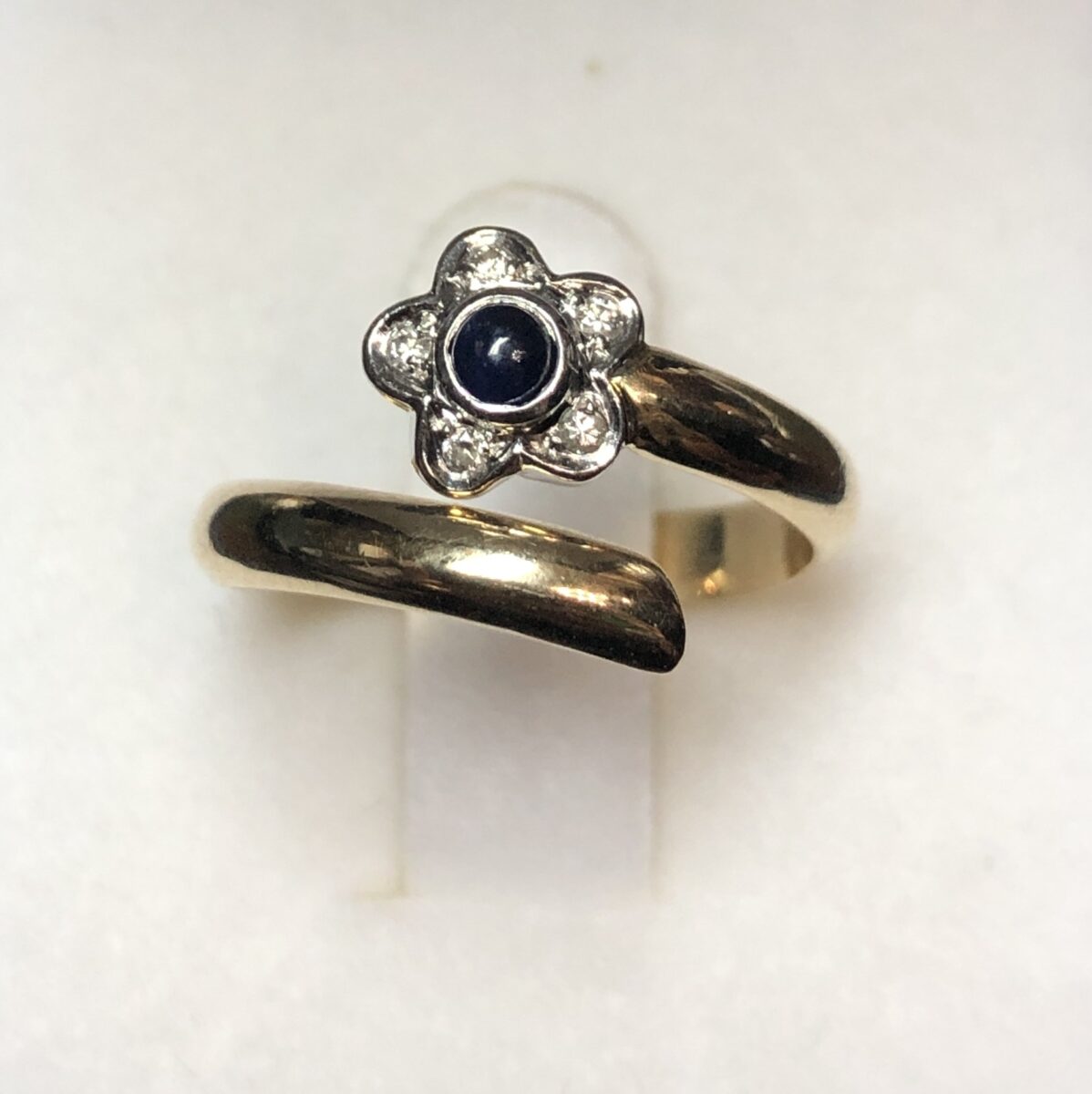 Sortija en forma de espiral con flor aderezada con brillantes y centro de zafiro natural, realizada en oro blanco y amarillo de ley 18 kts.