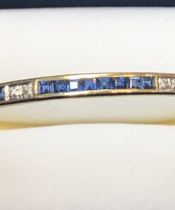 Pulsera de media caña con zafiros en carre y 0'05 cts de brillantes, realizada en oro amarillo de ley 18 kts.