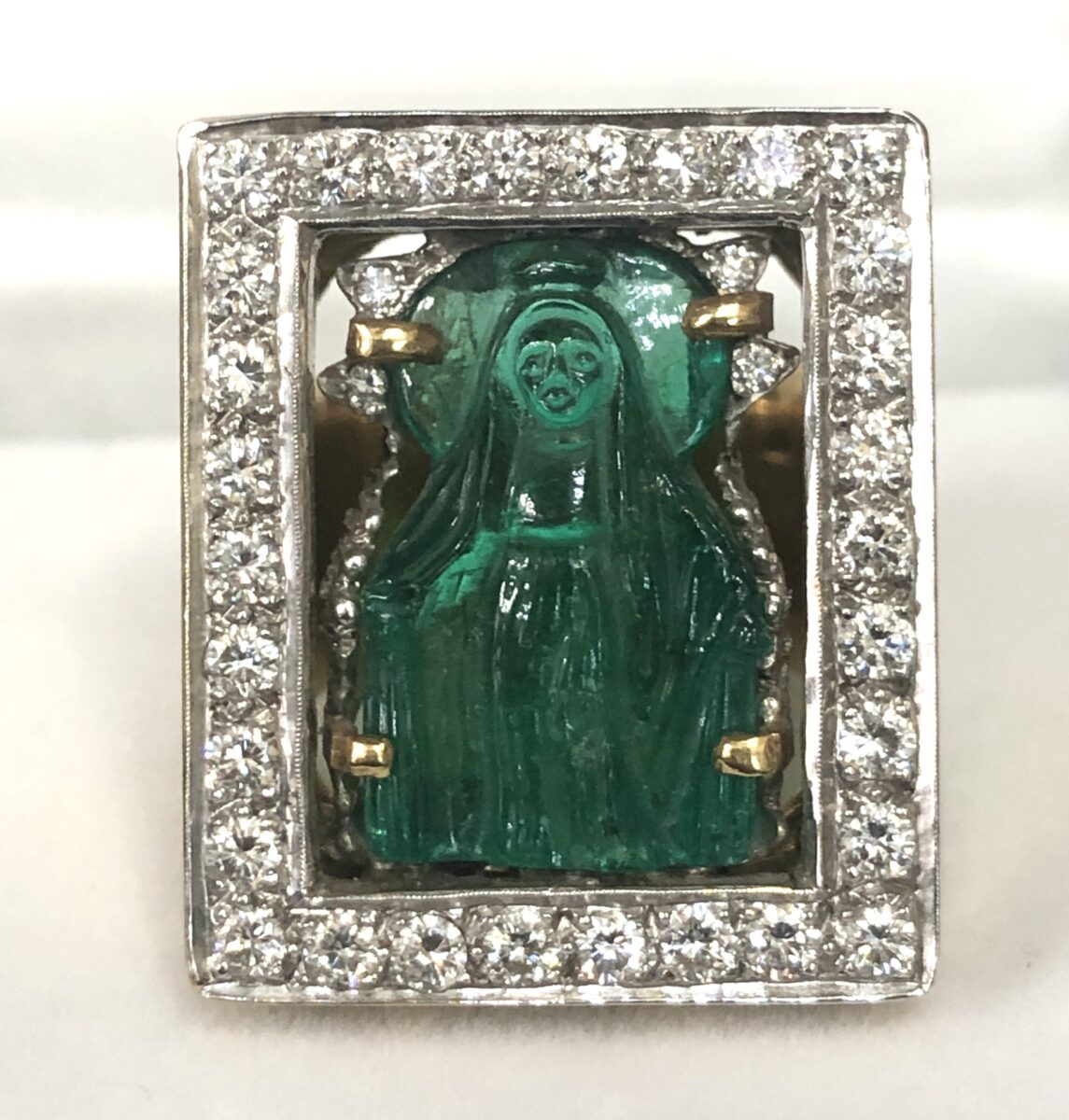 Gran sortija ancha con imagen de la Virgen tallada sobre esmeralda colombiana de 17 cts (aprox.) y enriquecida con 1'54 cts de brillantes, realizada en oro blanco y amarillo de ley 18 kts.