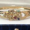 Bonito brazalete rígido con motivos florales, enriquecido con 0'90 cts de brillantes, y detalles de rubí, esmeralda y zafiro naturales. Realizado en oro amarillo de ley 18 kts.