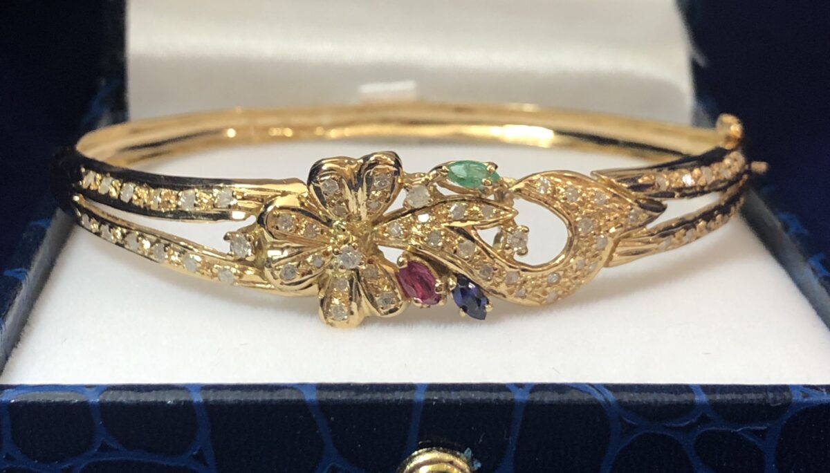 Bonito brazalete rígido con motivos florales, enriquecido con 0'90 cts de brillantes, y detalles de rubí, esmeralda y zafiro naturales. Realizado en oro amarillo de ley 18 kts.