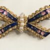 Bonito broche antiguo en forma de lazada con perlitas y esmalte al fuego con motivos florales, realizado en oro amarillo de ley 18 kts.