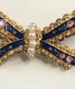Bonito broche antiguo en forma de lazada con perlitas y esmalte al fuego con motivos florales, realizado en oro amarillo de ley 18 kts.
