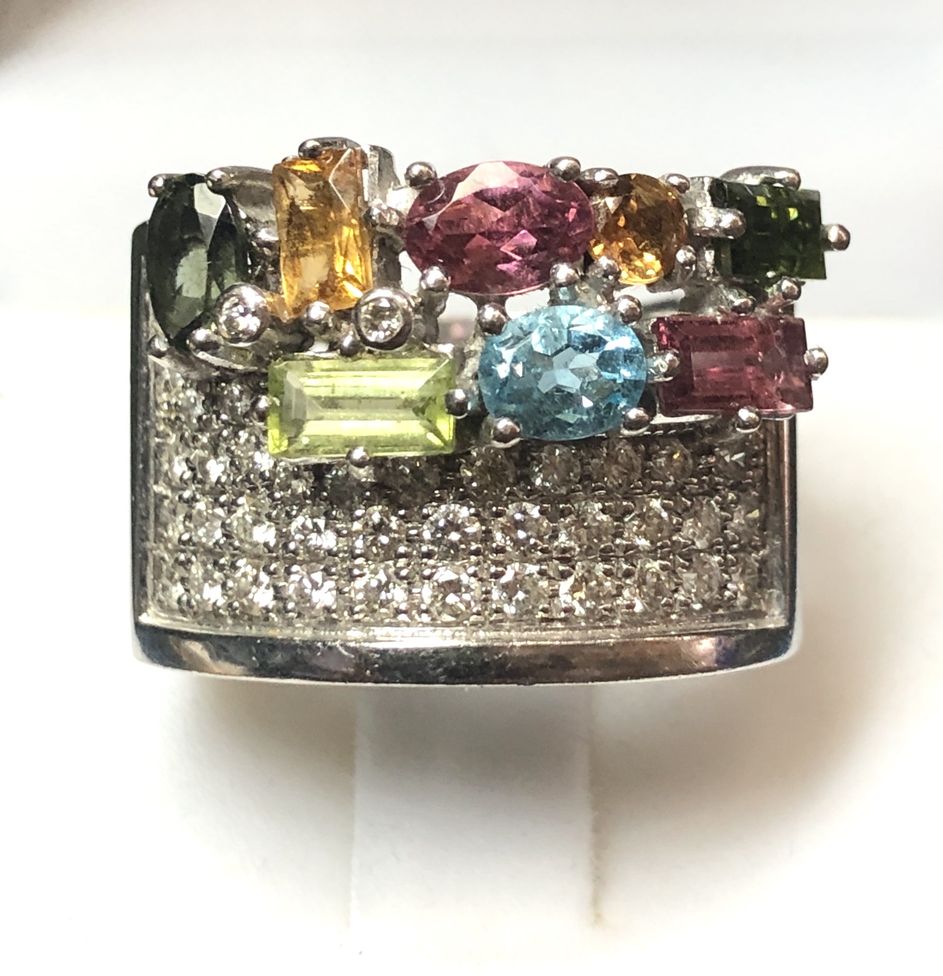 Sortija ancha con distintas gemas de colores y pavé de brillantes de 0'40 cts en total, realizada en oro blanco de ley 18 kts.