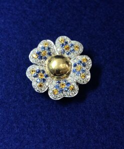 Broche en forma de flor cuajado de brillantes en pavé, zafiros y topacios, realizado en oro blanco de ley 18 kts.