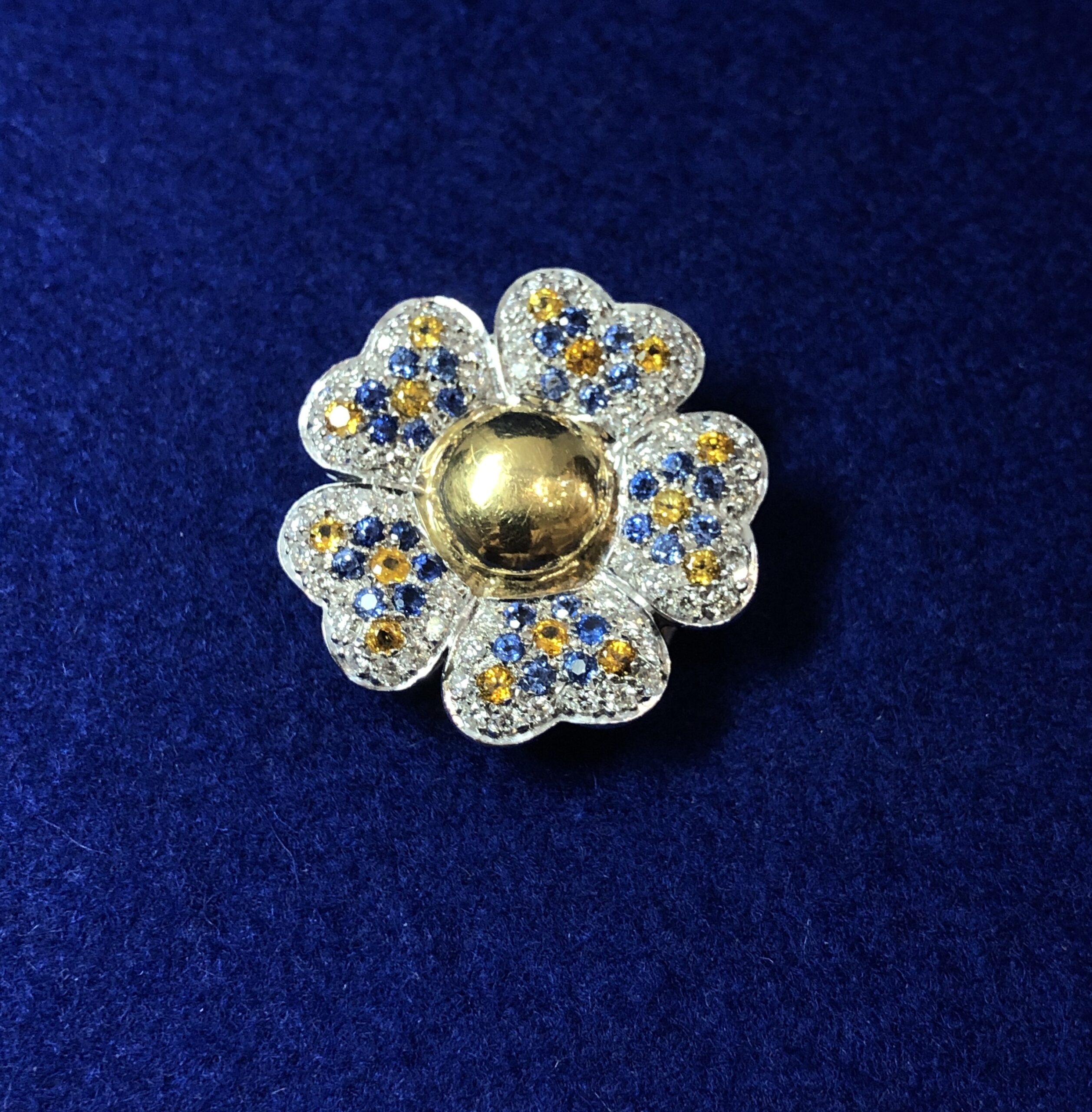 Broche en forma de flor cuajado de brillantes en pavé, zafiros y topacios, realizado en oro blanco de ley 18 kts.
